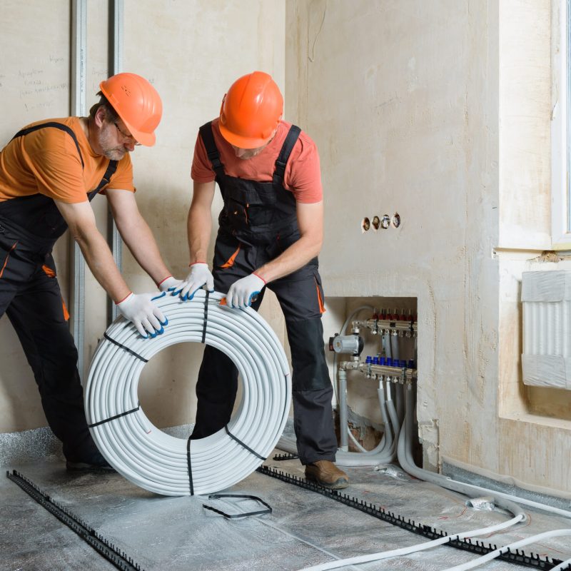 Workers are installing a pipe for the warm floor in the apartment. They are unpacking the tubes.