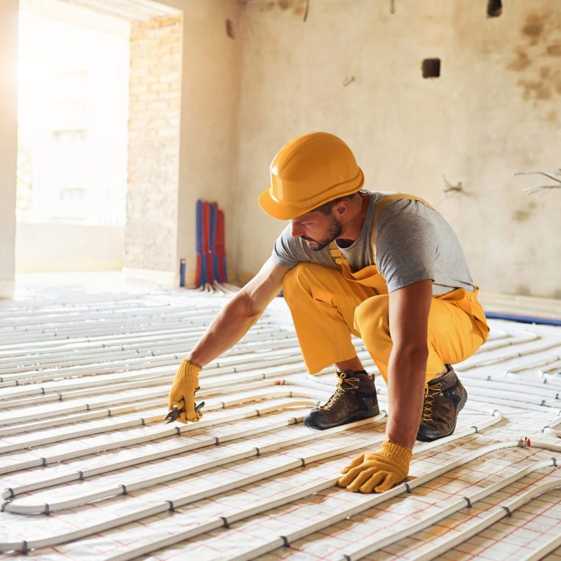Worker in yellow colored uniform installing underfloor heating system.