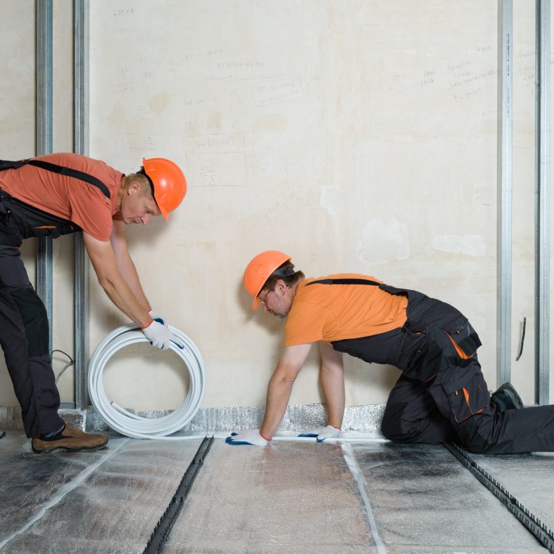Workers are installing a pipe for the warm floor in the apartment. They are unwinding tube.